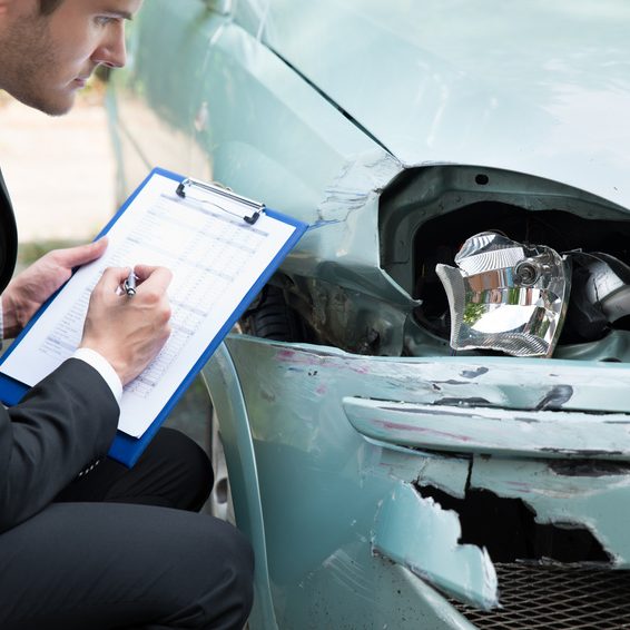 Insurance Agent Examining Car After Accident Side view of writing on clipboard while insurance agent examining car after accident